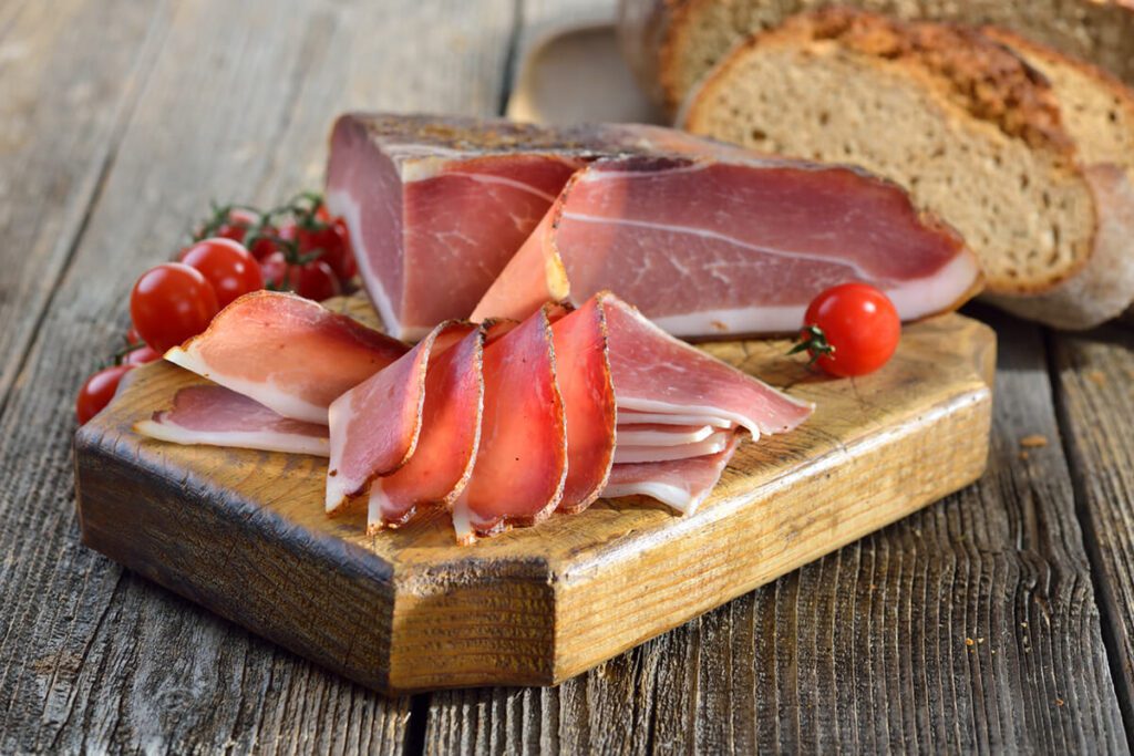 Tagliere con speck, fettine di speck tagliate e pomodorini